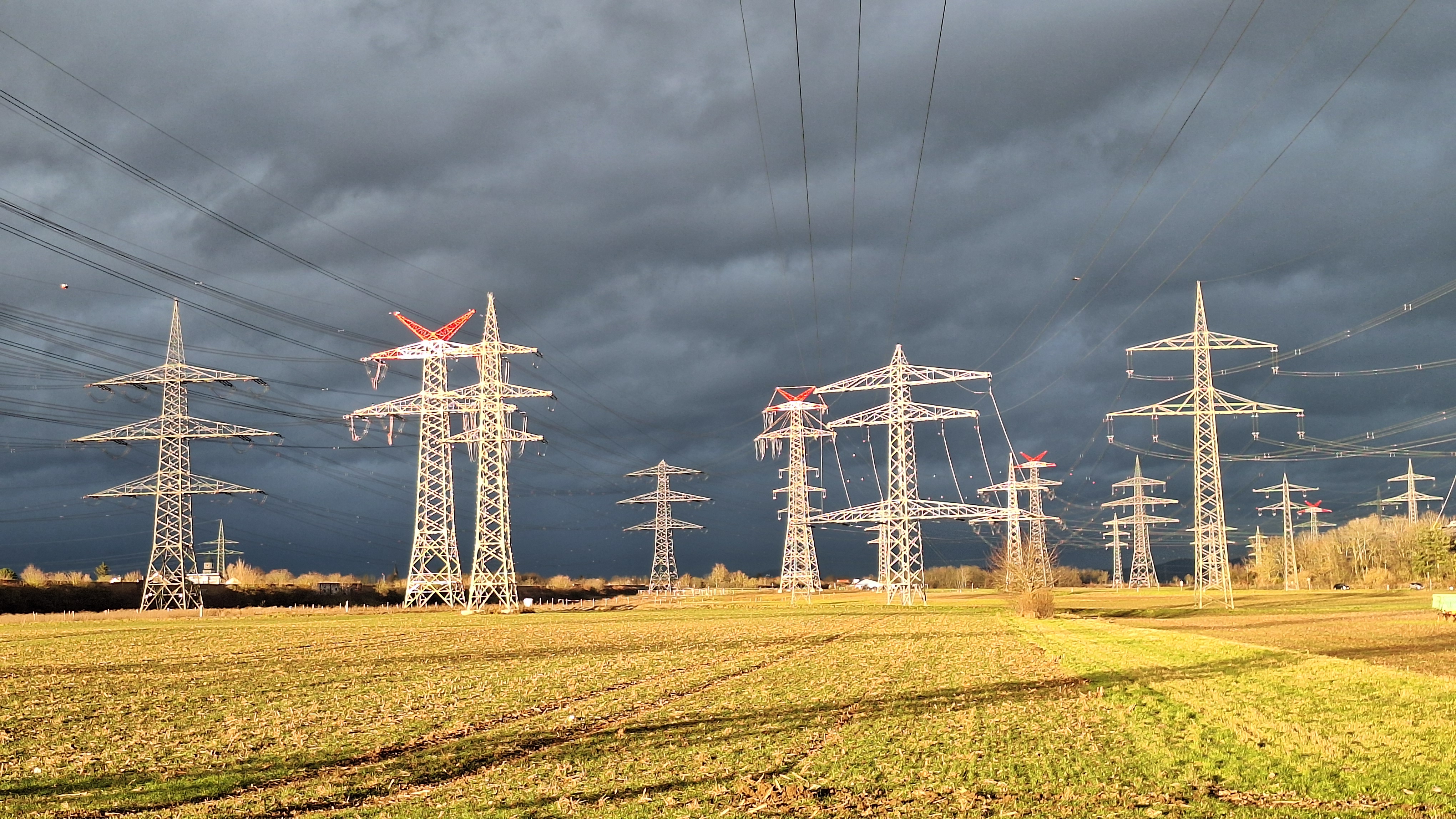 Leitungsstraßen Ilvesheim Hochspannungsmasten über einem Feld unter dunklen Gewitterwolken bei Ilvesheim